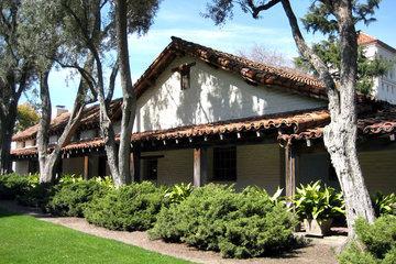 A traditional adobe lodge with a wooden veranda and lush greenery in the foreground.