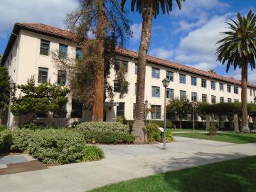 Kenna Hall building with surrounding trees and pathway on a sunny day.