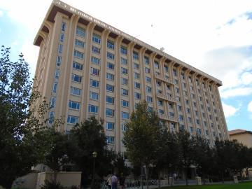 Tall building with numerous windows, surrounded by trees, titled 