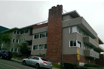 Three-story apartment building with a prominent brick chimney and parked car in front.