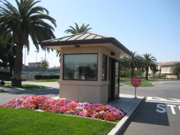 Small guard house beside a road with palm trees and flowers.