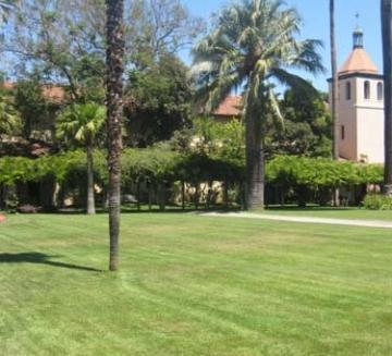 A green lawn with trees, bushes, and mission-style buildings in the background.