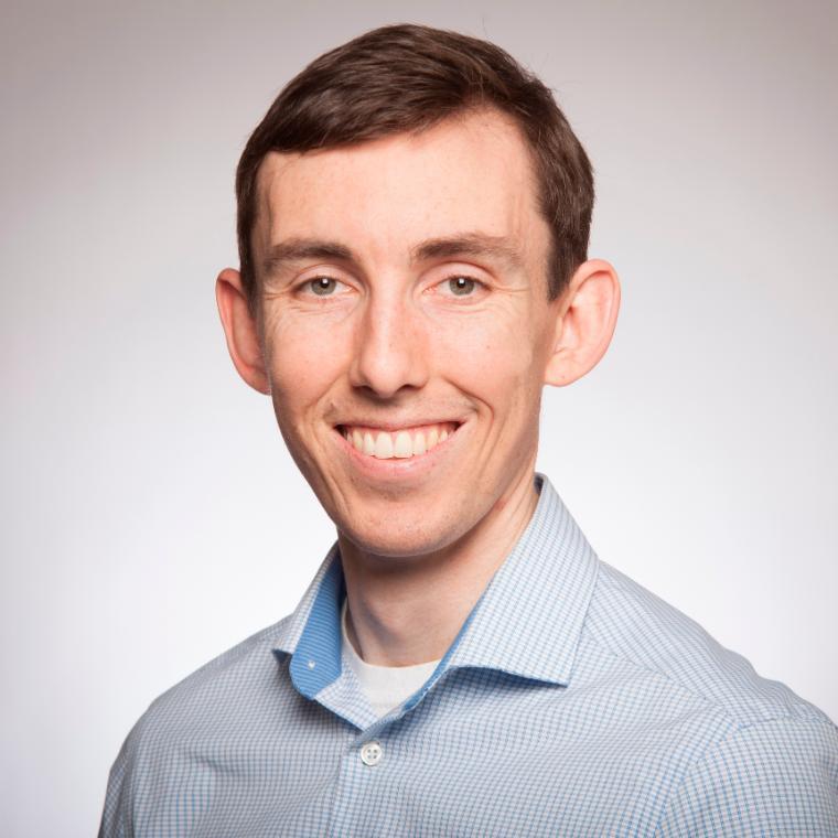 A person in a light blue collared shirt smiling.