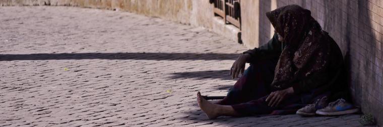 A person sitting by a wall in a shaded area.