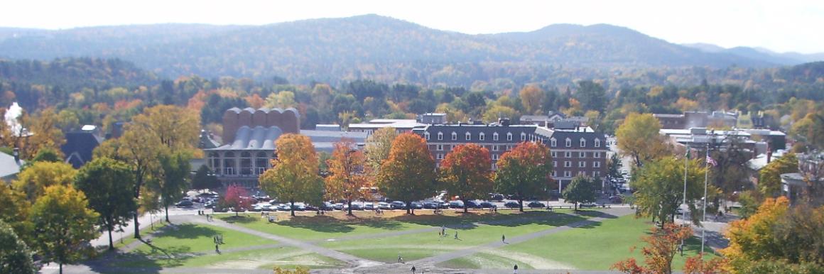 University campus with buildings, greenery, and mountains in the background on an overcast day.