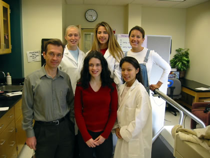 A group of six people, some in white coats, pose indoors.