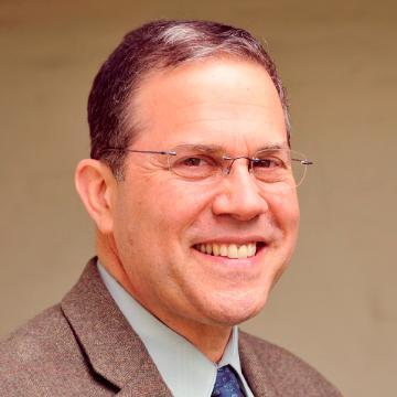 A man wearing glasses, smiling, and dressed in a suit and tie.