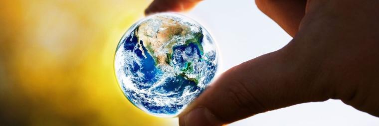 A hand holding a small globe between fingers.