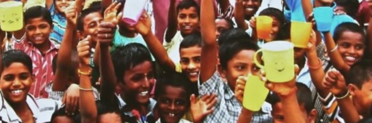 A large group of smiling children holding up handwritten notes.