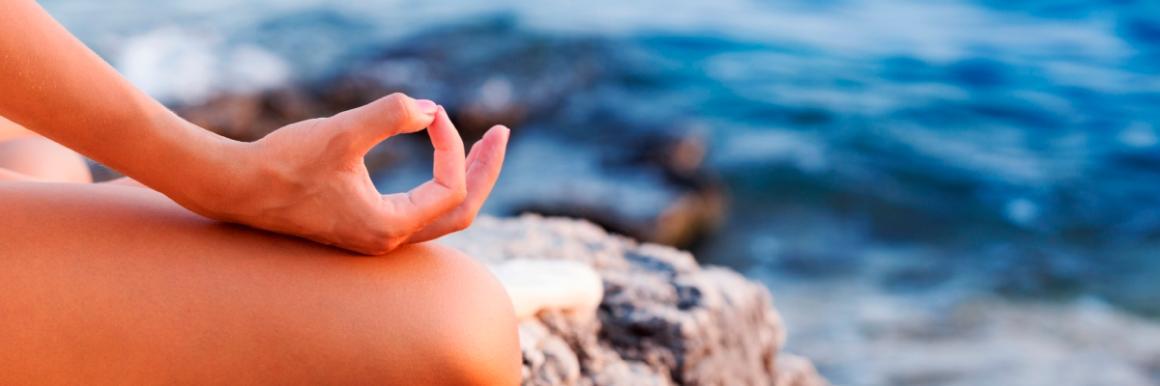 Person meditating with hand in yoga mudra by the ocean.