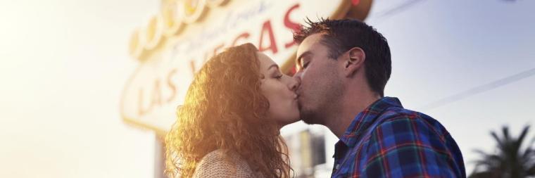 A couple kisses outdoors with sunlight in the background.