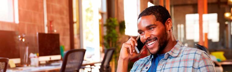 A person smiling while talking on a cellphone in an office.