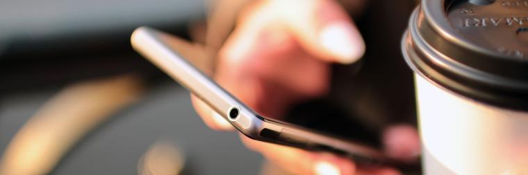 A person holding a smartphone and a coffee cup.