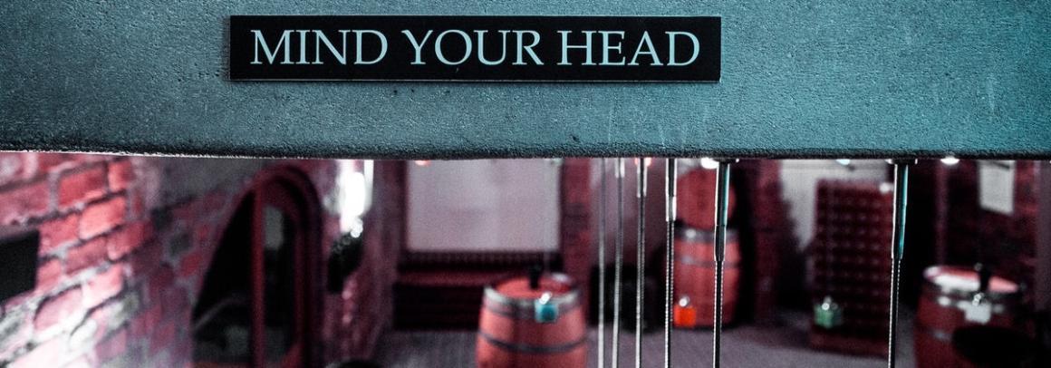 Photo of a low-hanging ceiling with MIND YOUR HEAD warning sign..