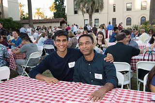 Two people sitting at a checkered tablecloth during an outdoor BBQ event.