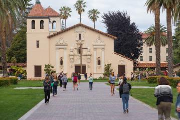 People walking on a path toward a historic mission building.