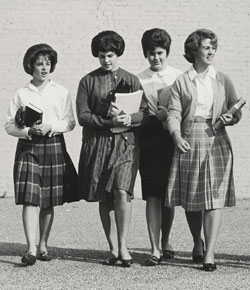 Four young women walking, carrying books, and dressed in 1960s style clothing.