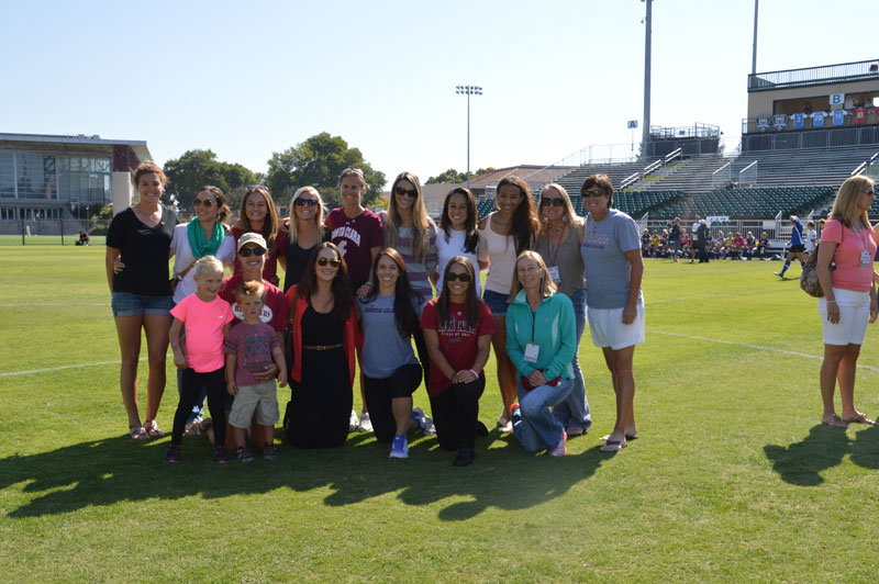 Group of people posing on a soccer field with stadium seats in the background.