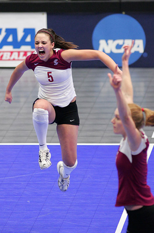 Two volleyball players celebrating on an indoor court, one jumping, with NCAA logo in background.
