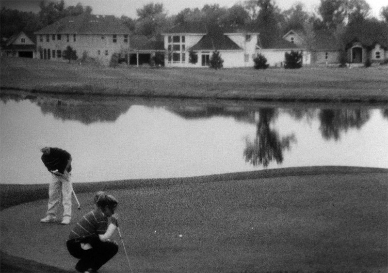 Golfer kneeling to read the green by a pond.