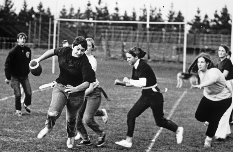 Black and white photo of women playing Powder Puff football in the 1970s.