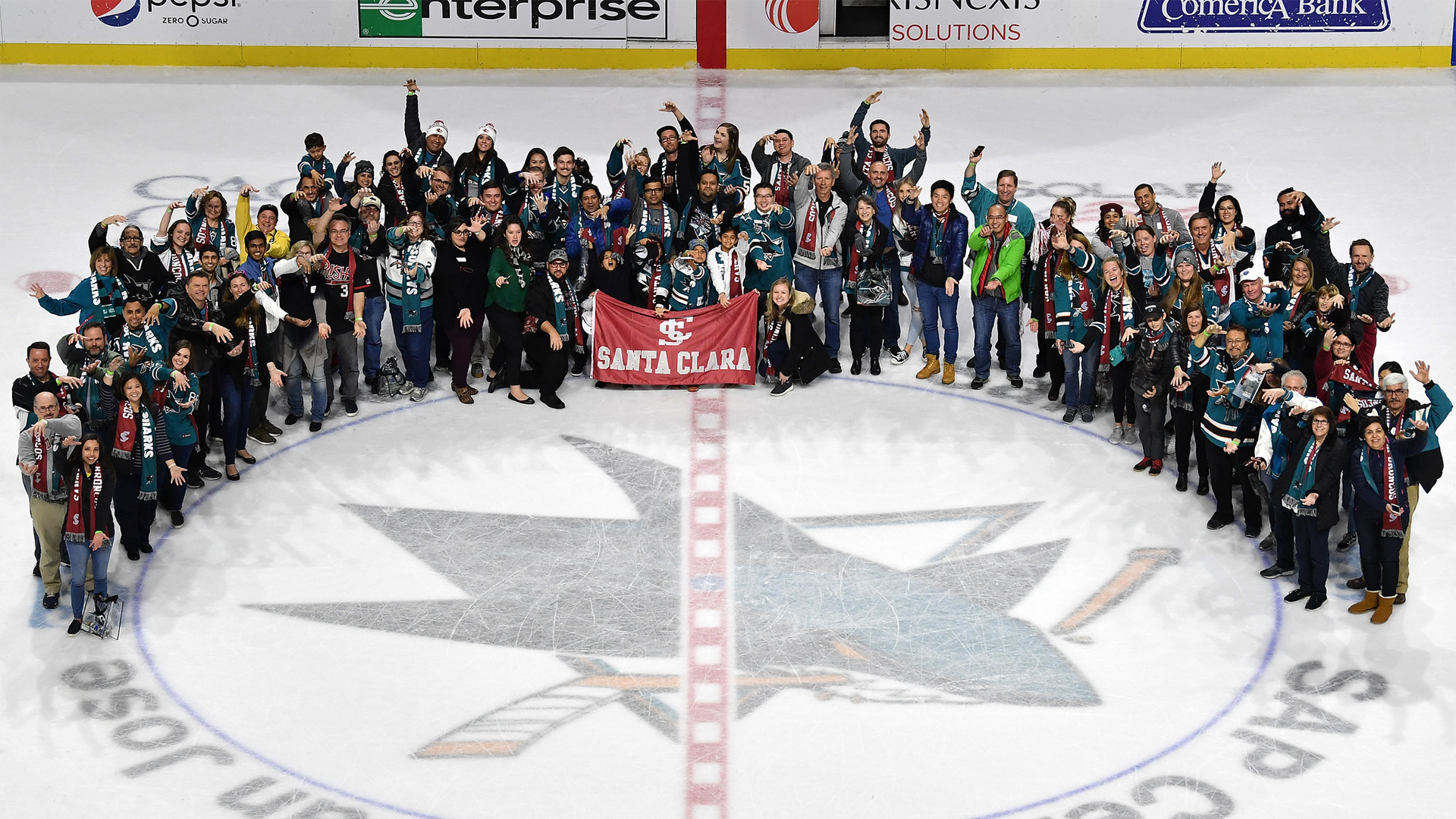 A large group of alumni gathered around an SCU banner at SAP Center