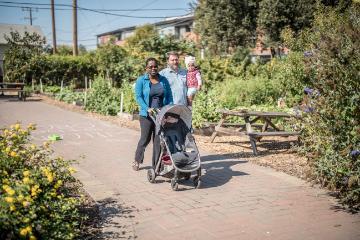 Two people standing on a garden path surrounded by lush greenery.