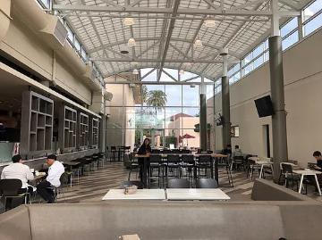 The photo shows people in a large, modern atrium with a glass ceiling.