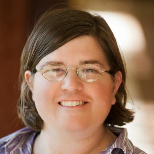 Woman smiling with glasses and a brown background.