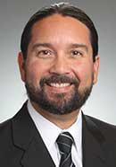 A man in a suit and tie smiling against a gray background.