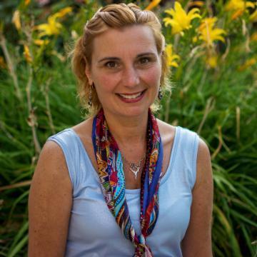 A person smiling, with greenery and yellow flowers in the background.