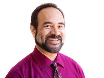 A man smiling in a magenta shirt and tie.