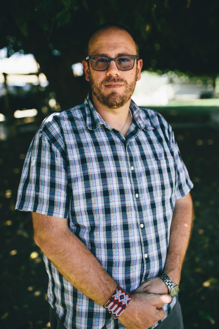 A person wearing sunglasses and a checkered shirt standing outdoors.