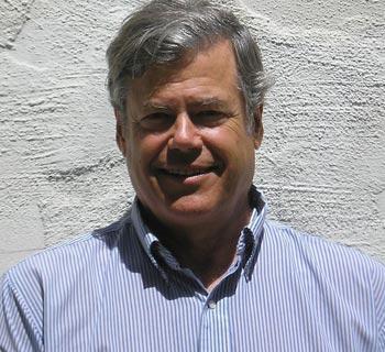 A man smiling in front of a white wall.