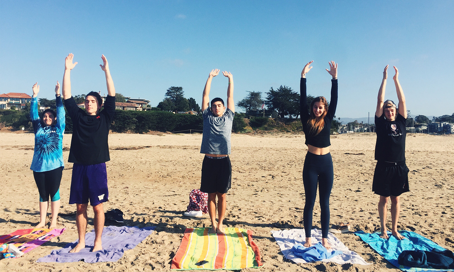 People doing yoga outdoors on mats with arms raised.