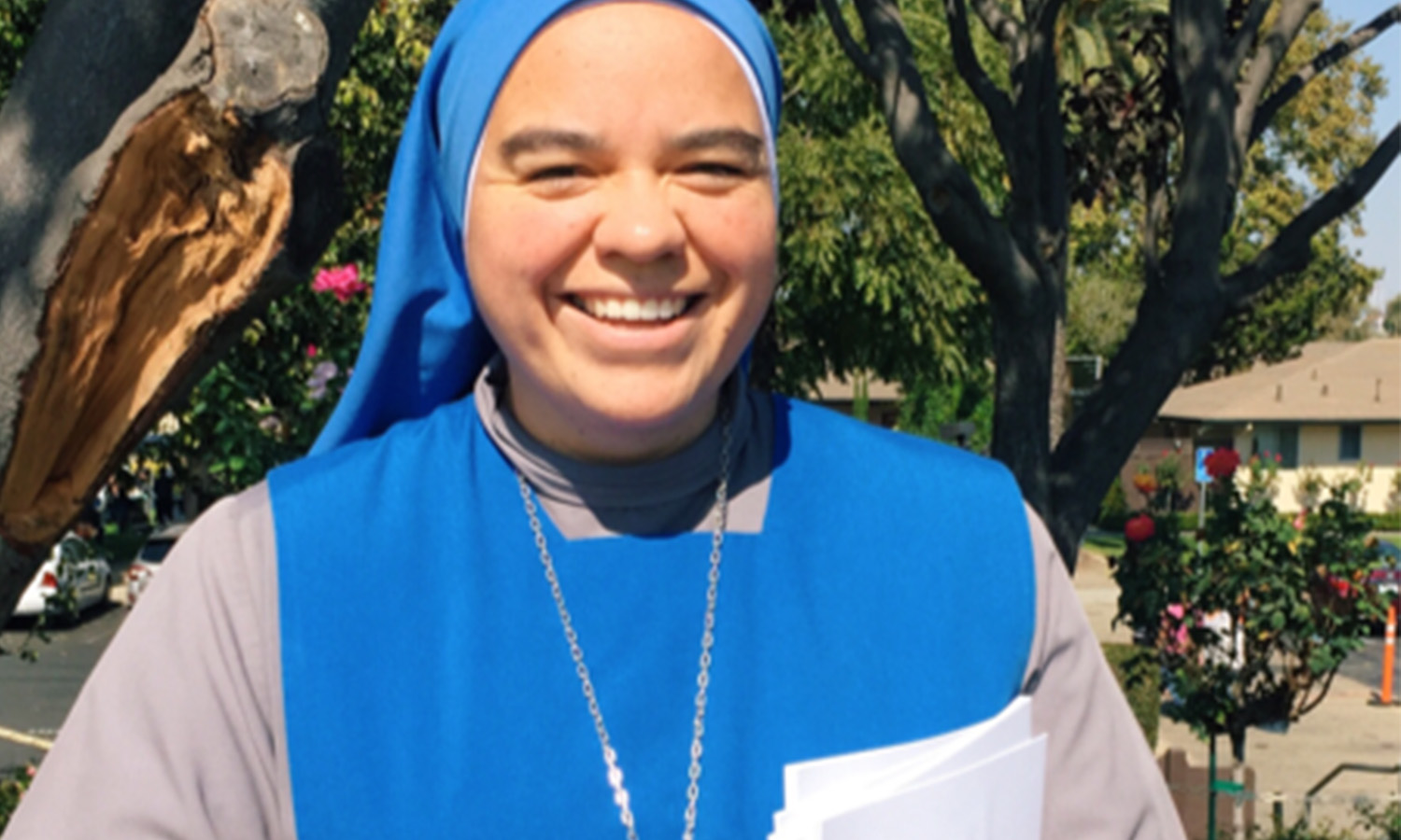 A person smiling wearing a blue religious habit outdoors.