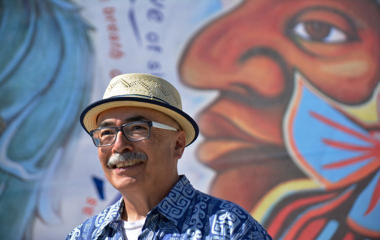 Juan Felipe Herrera standing in front of a colorful mural. image link to story