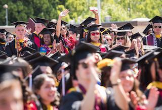 A large group of graduates in caps and gowns celebrating at commencement.