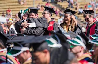 A group of graduates in caps and gowns hugging and celebrating.