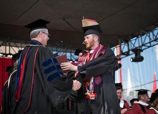 Two people in graduation attire shaking hands during a ceremony.