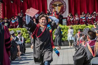 A graduate celebrating at a commencement ceremony holding a diploma.