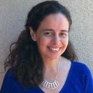 A woman smiling, wearing a blue top and necklace.