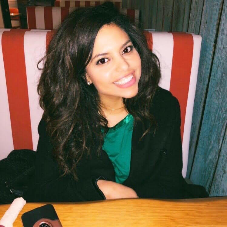 A person smiling while sitting at a table in a restaurant.