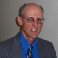 A man wearing glasses, a blue shirt, and a suit jacket.