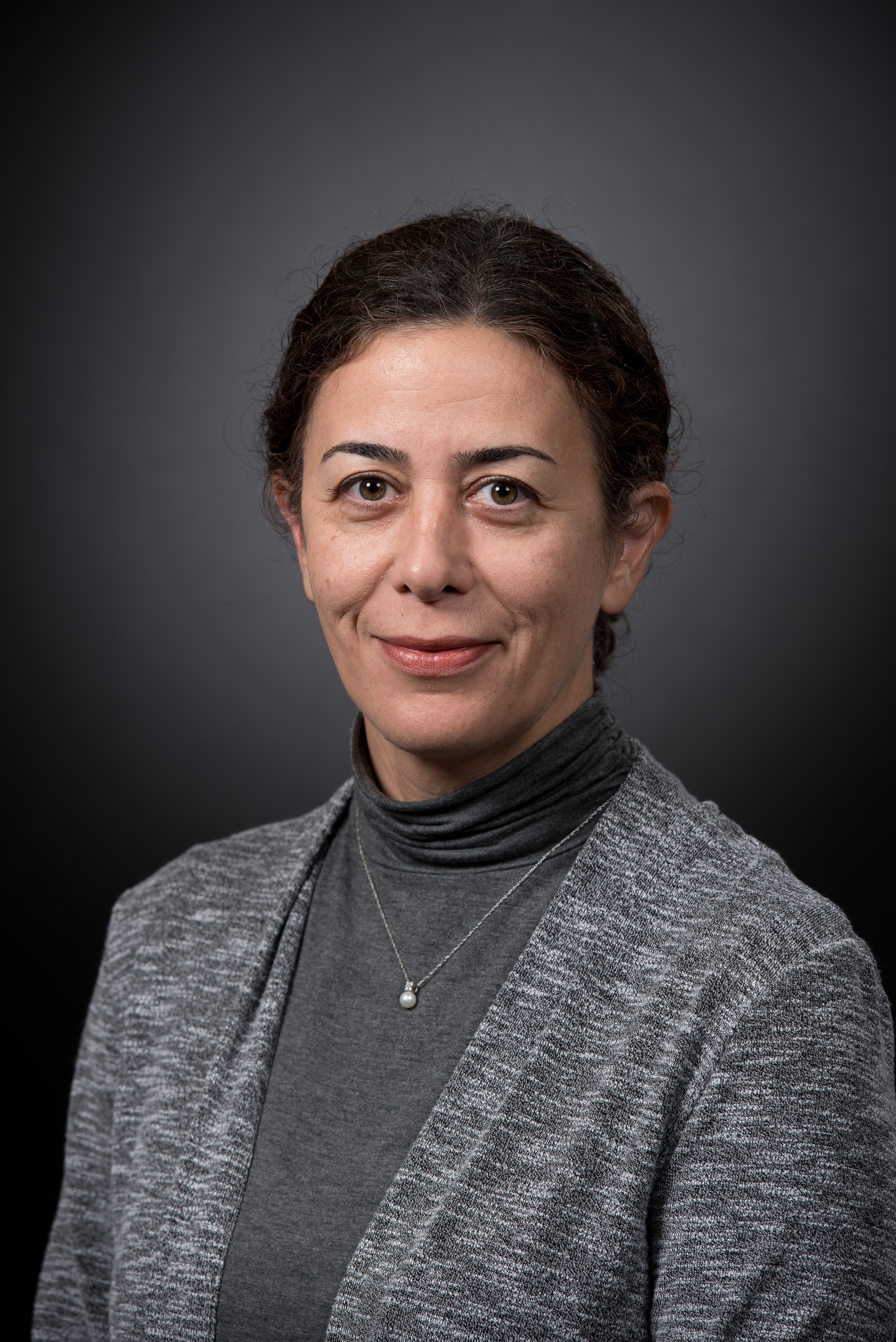 A person in a grey blazer against a dark background.