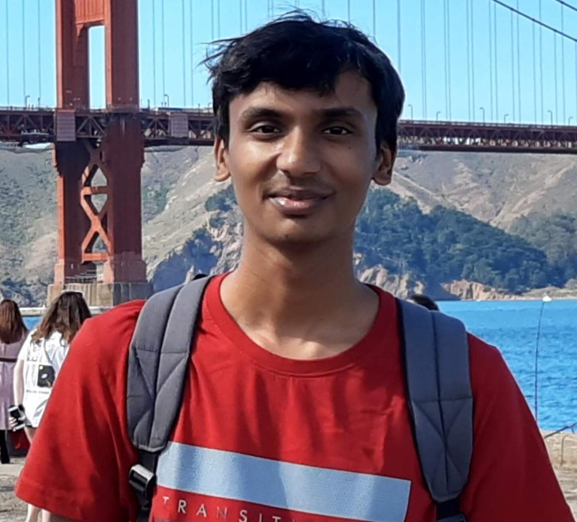 A person in a red shirt standing in front of the Golden Gate Bridge.