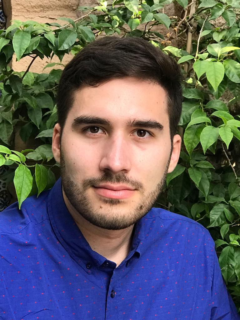 A man in a blue shirt against a leafy background.