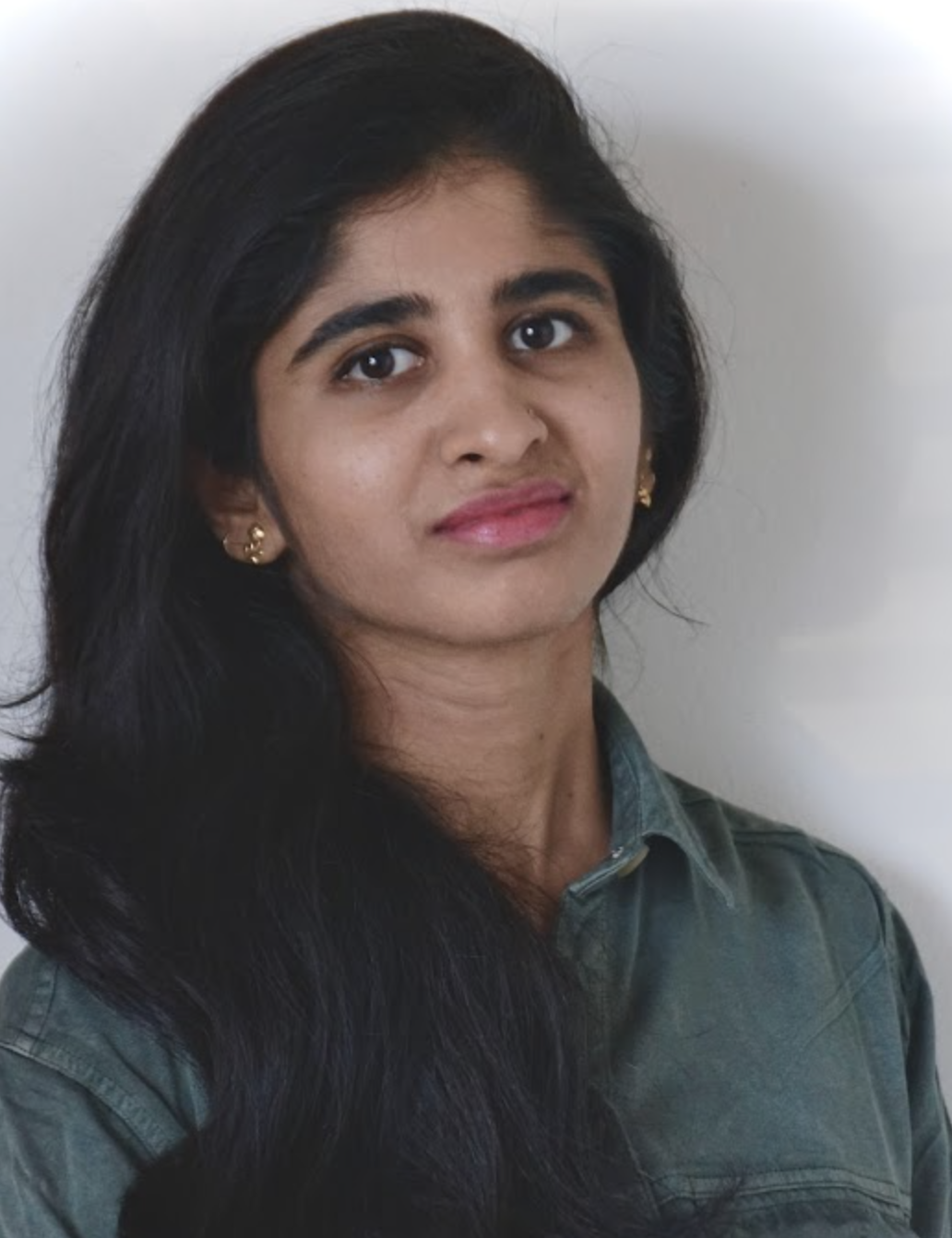 A woman with a neutral expression, wearing a green shirt, stands against a plain background.