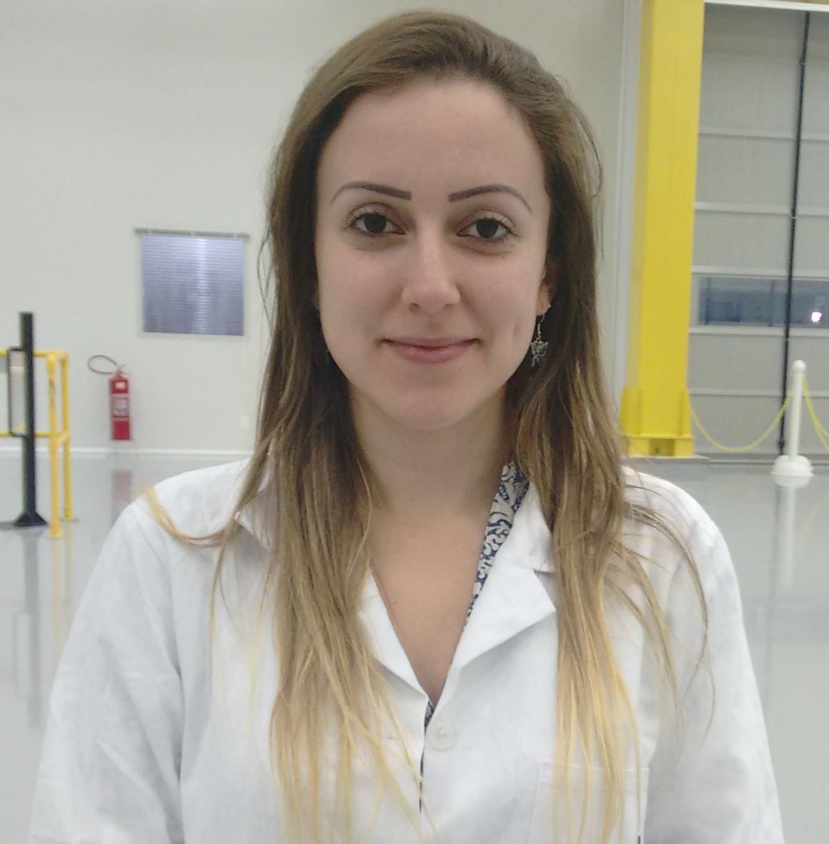 A woman in a white lab coat stands in a lab setting.