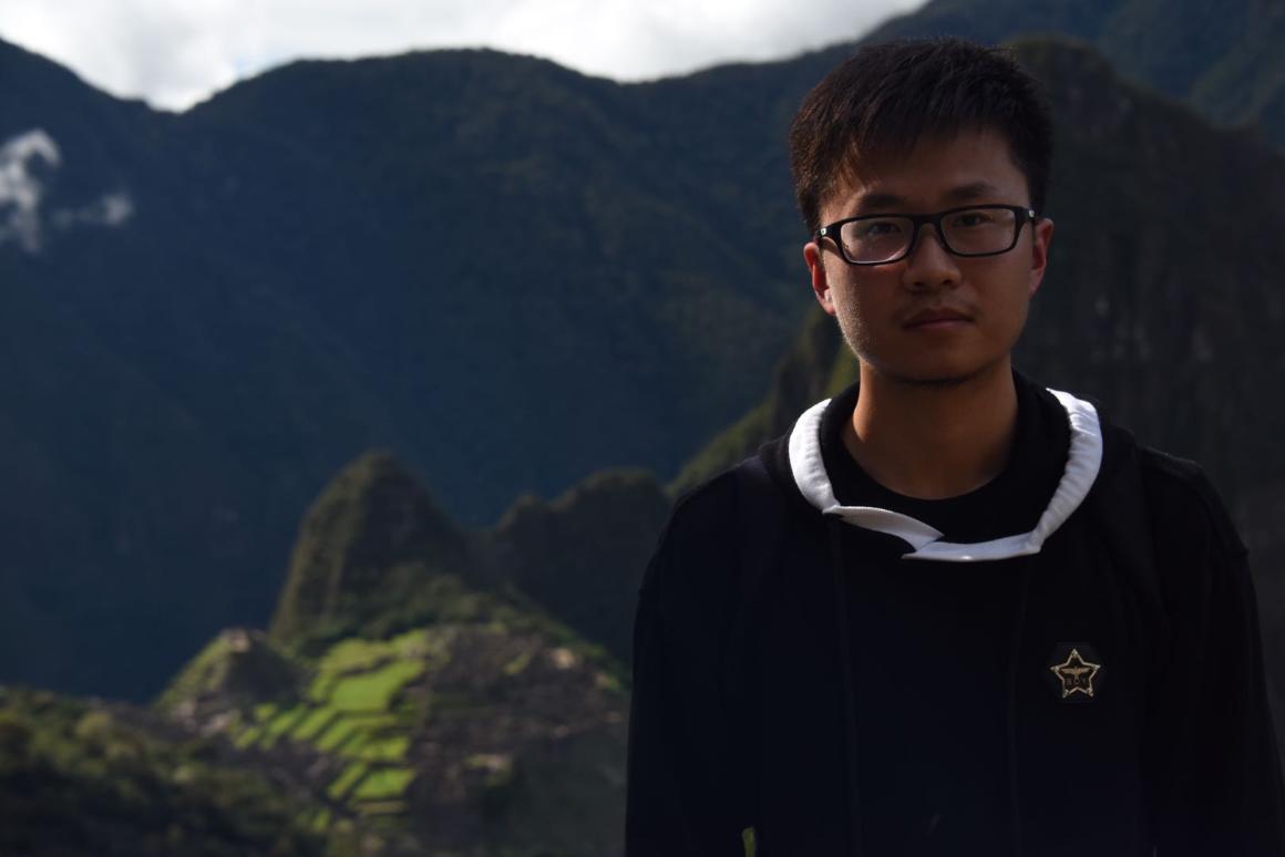 A person standing outdoors with a mountainous background.